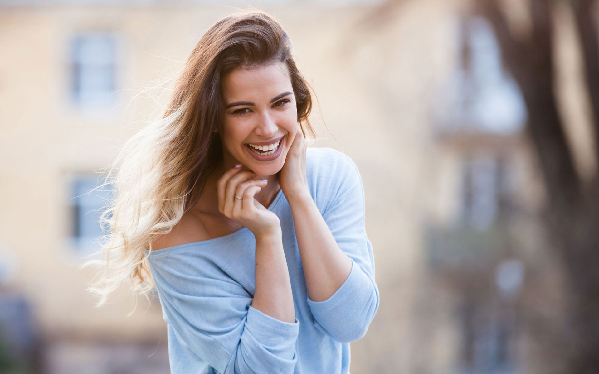 Moça jovem vestindo uma blusa azul de manga 3/4 rindo para a câmera