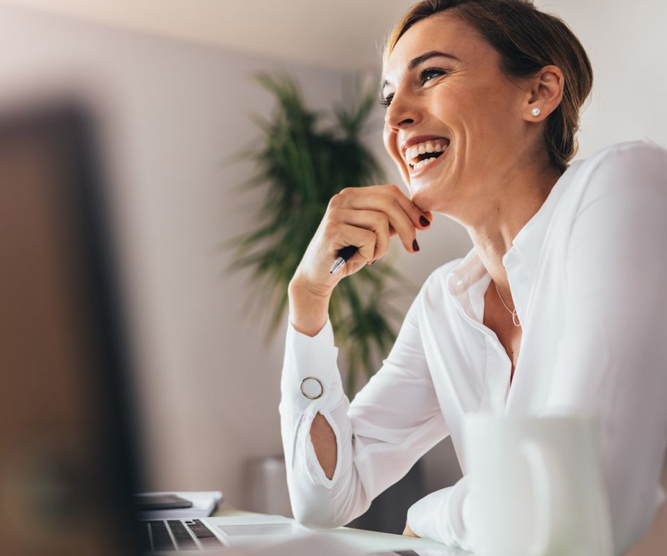 Mulher de meia idade, loira, com os cabelos presos, posicionada de lado, olhando para a frente e rindo.